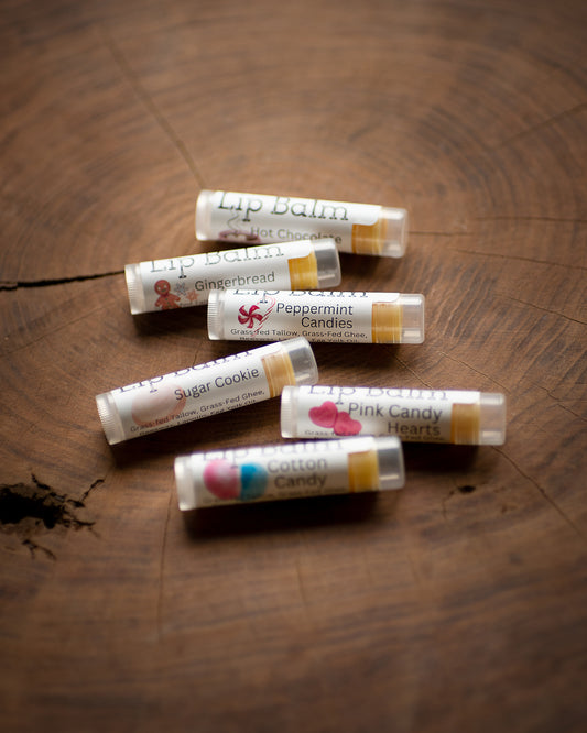 Six lip balm tubes sit on a tree stump, they are filled with a golden yellow lip balm made from grass fed tallow, grass fed ghee, egg yolk oil, and beeswax.  They come in many different flavors.